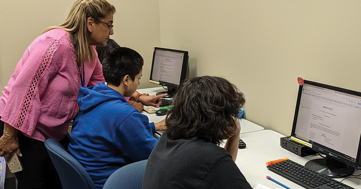 woman helping teenagers on computers