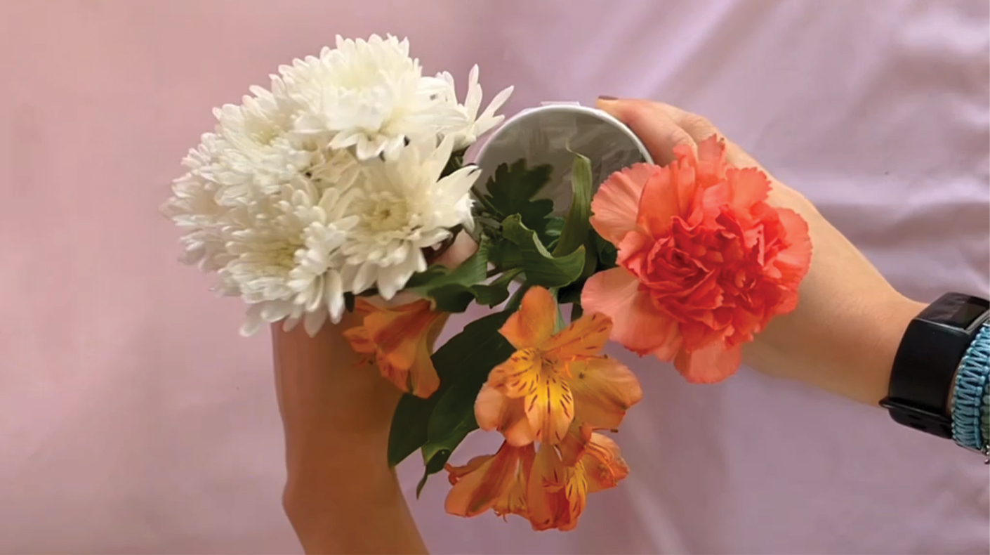 Hands holding a small bouquet of flowers in an upcycled vase