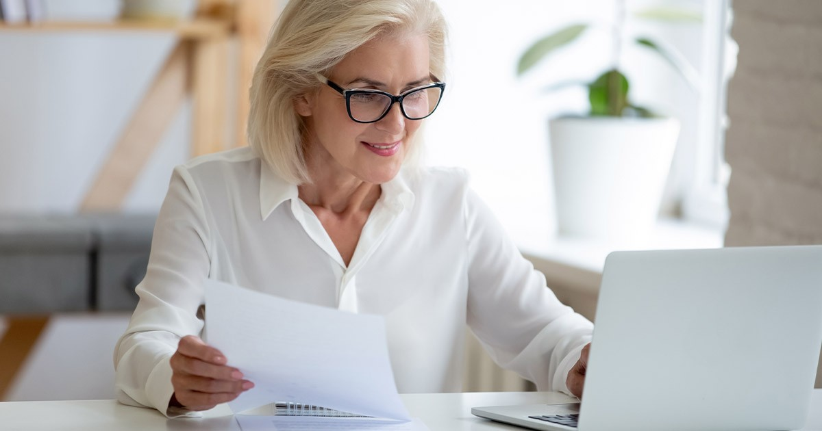 woman holding paper at laptop