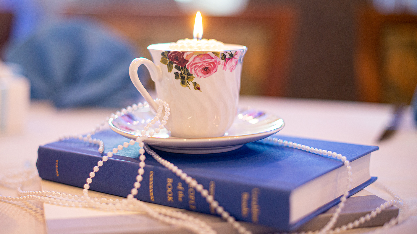 Thrifted Teacup Upcycled to a Candle Centerpiece A floral teacup candle sitting atop a book and faux pearls