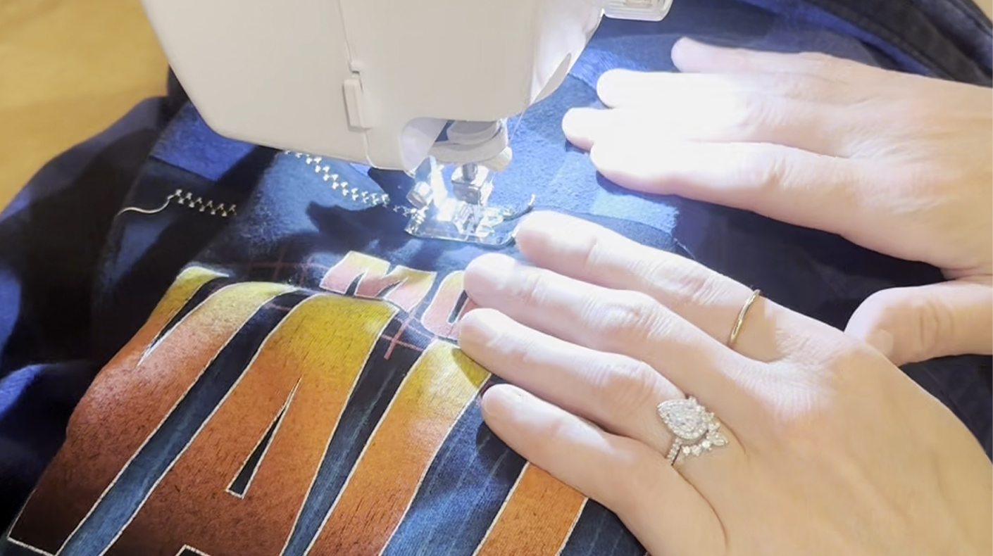 Hands moving a graphic shirt under a sewing machine