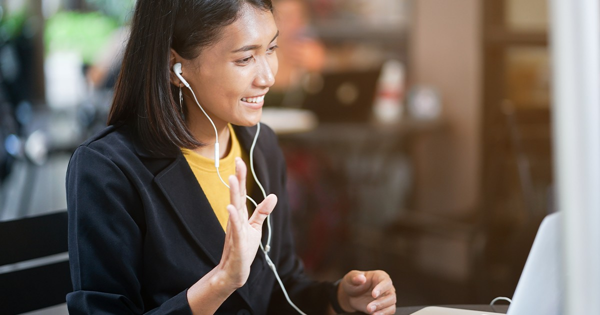 woman wearing earbuds waving at computer screen