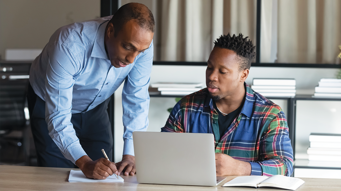 man helping another man write a resume on a laptop