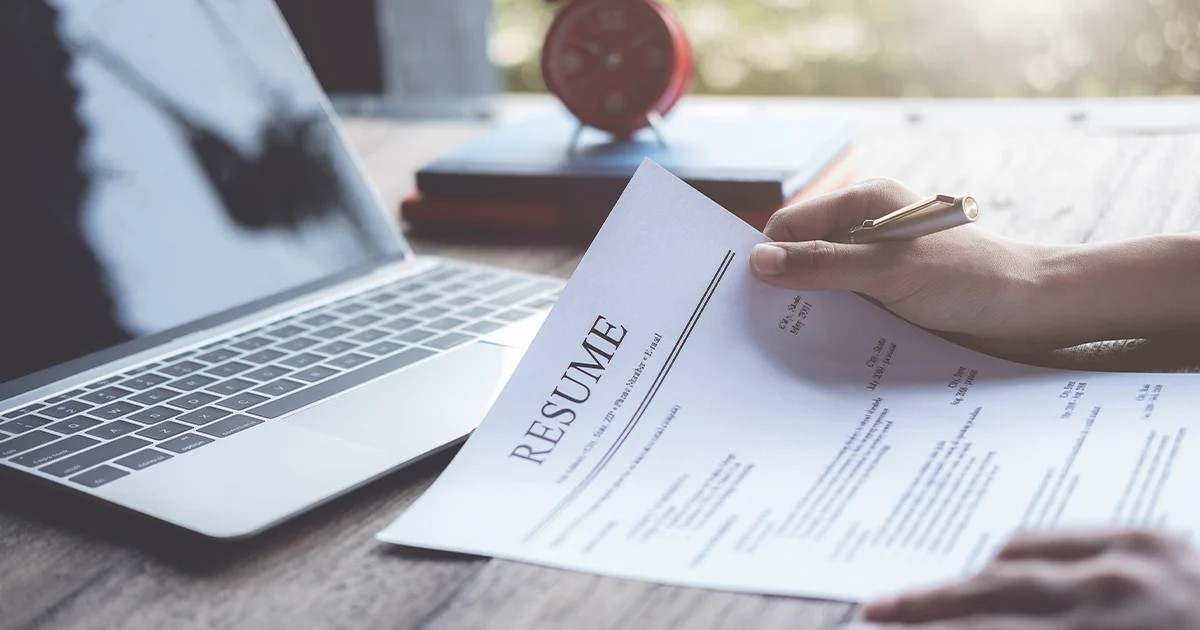 person holding resume in front of laptop