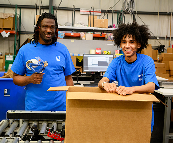two goodwill workers standing by a box they are packing