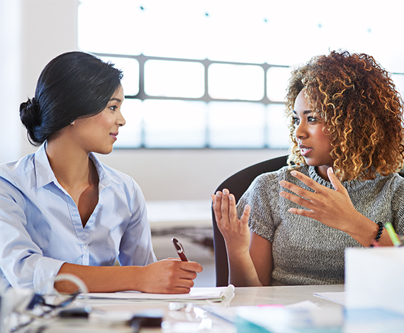Two women in a business meeting. The woman on the left is taking notes.