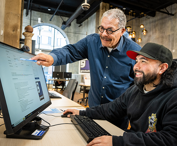 Two men at a workforce connection center working on a computer. One is pointing at the screen the other is typing